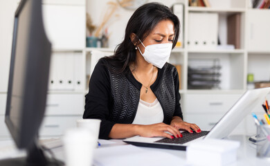 Busy female entrepreneur in medical mask at office desk