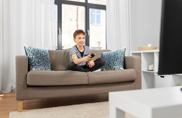 Fototapeta premium people and childhood concept - happy smiling boy with remote control watching tv girl sitting on sofa at home