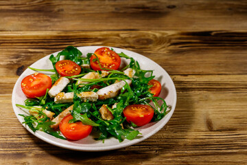 Tasty salad of fried chicken breast, fresh arugula and cherry tomatoes on wooden table