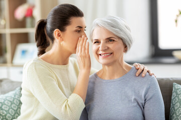 family, generation and people concept - adult daughter whispering secret to happy smiling senior mother at home