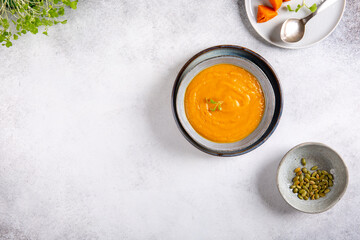 Vegetable cream soup in gray bowl on concrete background.  Sweet potato soup served with herbs and pumpkin seeds.