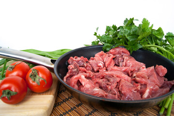 Fresh raw chopped beef in a pan with tomato and herbs on the kitchen table