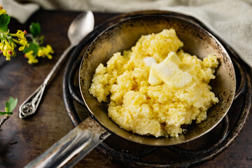 Hot corn porridge with sugar and butter on an old rustic pan and a metal vintage stand. Next to it is a sprig of flowering black currant with yellow flowers