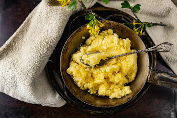 Hot corn porridge with sugar and butter on an old rustic pan and a metal vintage stand. Next to it is a sprig of flowering black currant with yellow flowers