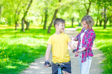 Mom spraying insect repellent or sunscreen lotion on skin her son, who ride a bike at summer park. Empty space for text