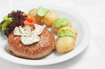 Meat cutlet with boiled potatoes and vegetables on a white plate.