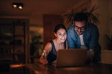 Happy couple at home, watching videos online on laptop, portrait.