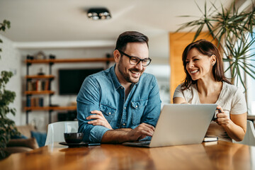 Happy couple at home, using laptop, portrait.