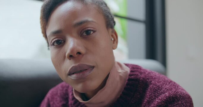 closeup and moving shoot of a young african woman sitting on the couch staring the camera a lady looking at the shot with no expression  on sofa at home
