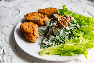 Colorful delicious dish with a salad of sorrel and sour cream, topped with fried sesame seeds, next to fried steaks of red fish pink salmon in breadcrumbs