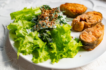 Colorful delicious dish with a salad of sorrel and sour cream, topped with fried sesame seeds, next to fried steaks of red fish pink salmon in breadcrumbs