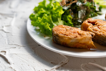 Colorful delicious dish with a salad of sorrel and sour cream, topped with fried sesame seeds, next to fried steaks of red fish pink salmon in breadcrumbs