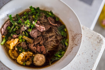 Asian noodles with cooked beef in traditional ceramic bowl. Thai peoples call Boat Noodles.