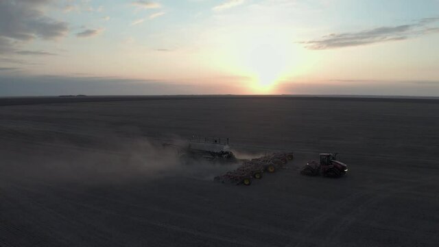 Farmer Driving A Tractor Seeding On The Field At Sunrise In Saskatchewan, Canada. - aerial drone shot