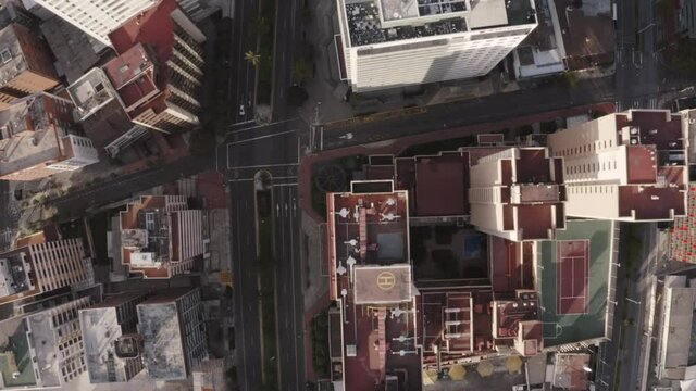 Drone shot of rooftops of houses and buildings in Avenue twelve of October in the city of Quito, Ecuador during quarantine. Overlooking empty streets with trees and no cars.