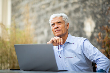 Obraz premium businessman sitting outside with laptop looking away