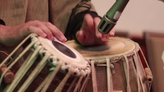 Medium close up of a mans hands tapping out a rhythm on a pair of tabla drums