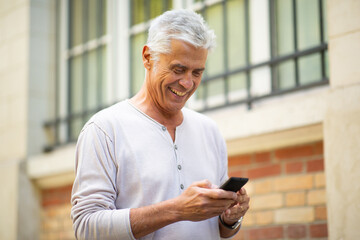 happy older man looking at mobile phone in city