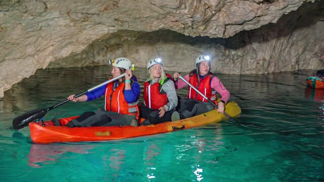 Caucasian friends on kayaks in underground rocky cavern, paddle through clear pristine water, Podzemlje Pece, Mezica, Slovenia, slow motion pan