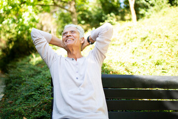 handsome older man relaxing in park with hands behind head