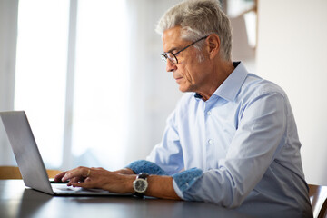 Side of businessman with glasses sitting at office desk using laptop comp[uter