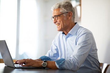 Close up side of smiling businessman sitting at office desk using laptop computer