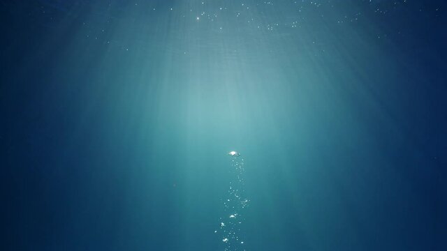 Sunlight beams shining through the deep crystal clear blue-turquoise colored water causing a beautiful lighting reflections curtain with air bubbles rising up to the water surface