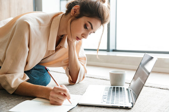 Image of woman writing down notes and using laptop while sitting on floor