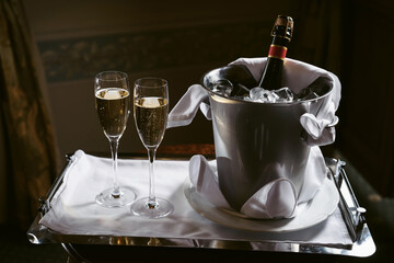 A bottle of champagne in an ice bucket and two glasses nearby. Luxury Hotel Room, Welcome Compliment for Guests