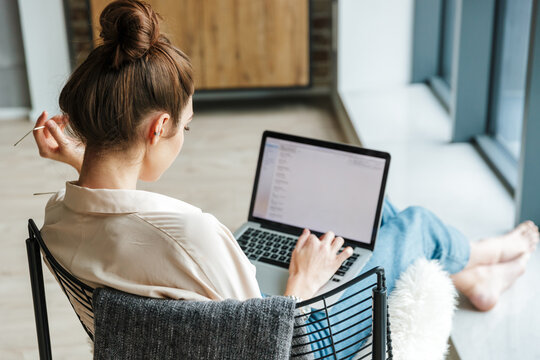 Image of focused woman working with laptop while sitting in armchair