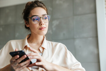 Fototapeta premium Image of pleased woman using mobile phone while sitting on couch