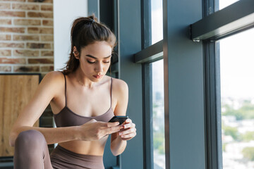 Naklejka na ściany i meble Image of young athletic woman using mobile phone while working out