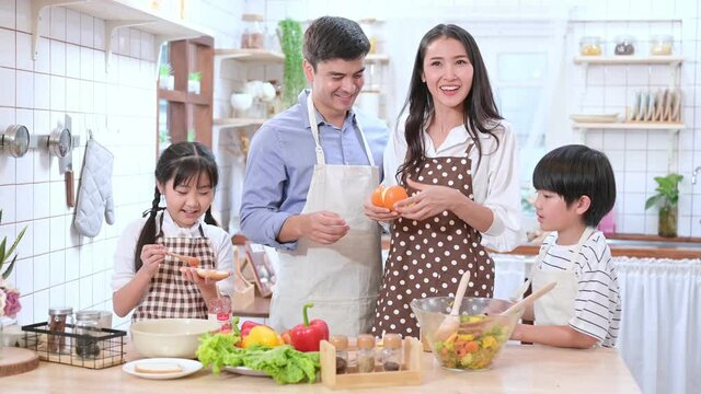 Happy family of Caucasian husband and Asian wife with their son and daughter cooking together in the kitchen happily.