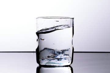 Water in a glass with curved upper surface after a splash. White background