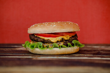 Cheeseburger on wooden table with red background. Homemade cheeseburger. Can be used for restaurant, cafe, food truck menu. Burger for ads. Burger for bigboard. Cheeseburger with 2 meat. Fast food. 