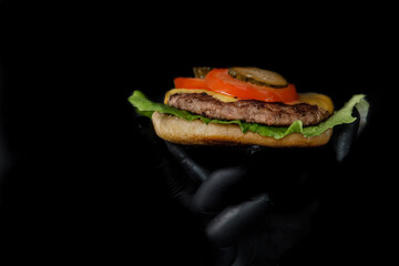 Homemade burger.Meat for burger with black background. Meat for bufger with cheese and tomato. Isolated meat for burger with dark background. Fast food. Hand holds burger. Can be used for ads, menu.