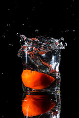A glass of water in a dark background and water being splashed with a piece of cut tomato dropped inside the glass