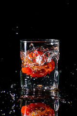 A glass of water in a dark background and water being splashed with a piece of cut tomato dropped inside the glass