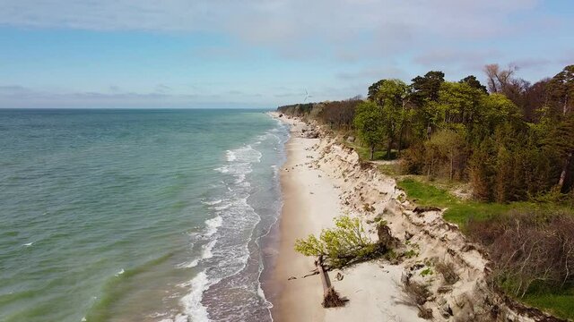 Aerial view of Baltic sea coast in sunny day, steep seashore dunes damaged by waves, coastal erosion, climate changes, wide angle drone shot moving forward