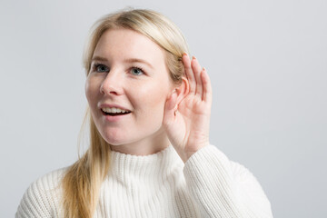 Young happy woman with hand at her ear tries to listen better