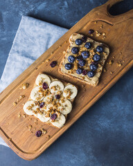 Dessert of sweet bread with banana,peanut butter, blueberries and granola on the top.