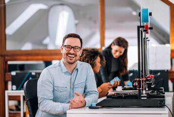 Fototapeta na wymiar Portrait of a happy engineer with 3D printer, looking at camera.