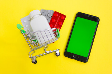 Online pharmacy. Closeup of hands on a phone and a mini shopping trolley with tablets. A woman chooses medicines on the Internet with home delivery