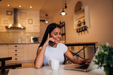 Young smiling woman working from home, using laptop and smart phone, portrait.