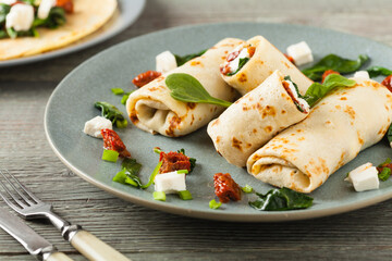 Pancakes with spinach, feta and dried tomatoes. Served on a gray plate. Wooden natural background.
