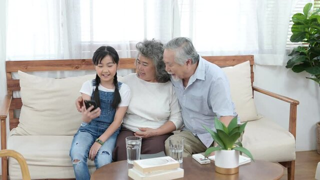 Asian cute girl taking selfie photo with her grandparent in living room of her home.