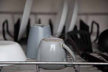 gray ceramic coffee cup on the metal grid of a dishwasher. defocused cups, plates, spatula and whisk in the background. selective focus