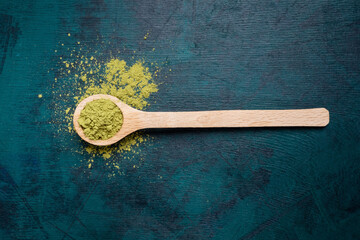 Wooden spoon filled with green matcha tea powder with a little bit powder spilled out on emerald backdrop. Japanese Matcha tea is luxury organic beverage rich of antioxidants. Top view. Copy space.