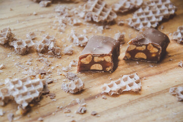 Close up picture of chocolate candy cut on parts on wooden background with waffles on sides, bar with peanuts and nougat covered with milk chocolate, as home made food photography and concept
