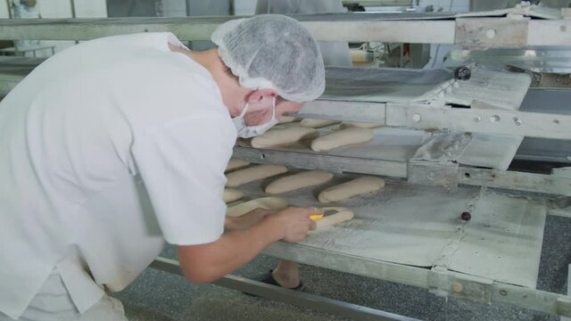 Bakery baking bakery. The worker makes patterns on the buns with a baking knife.
